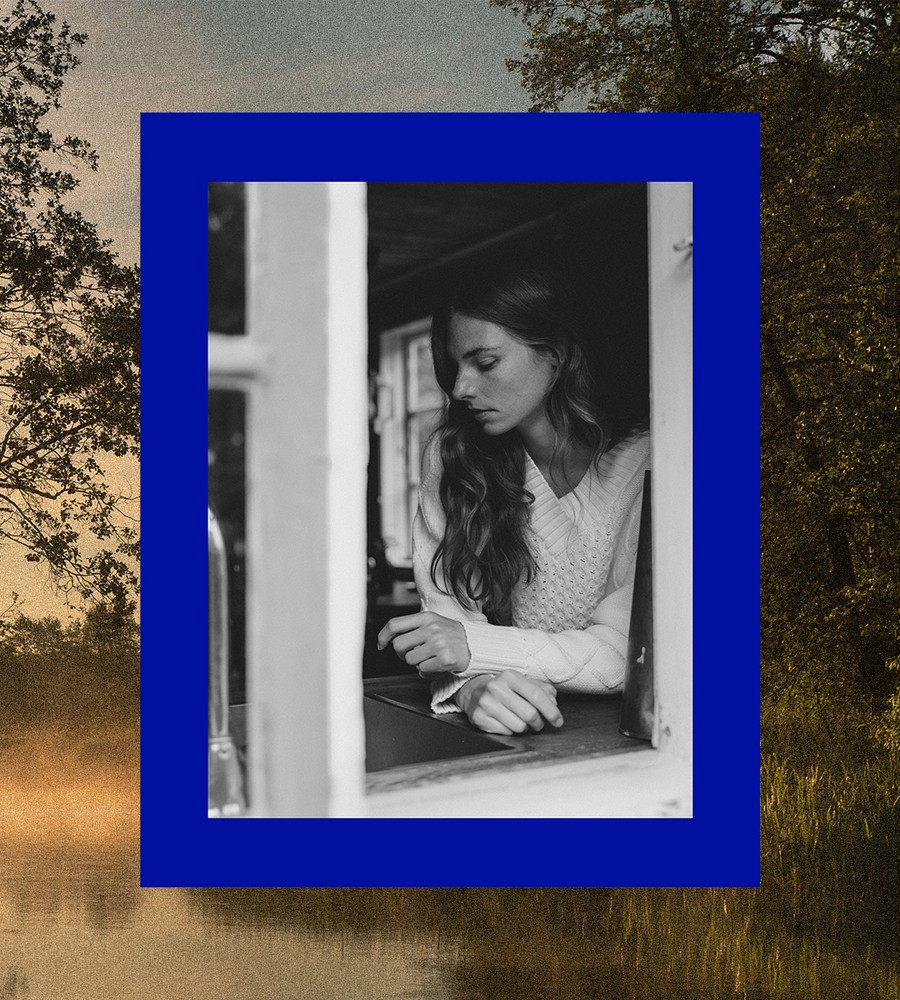 Kvinna går längst med havet i gräset och bär linneplagg