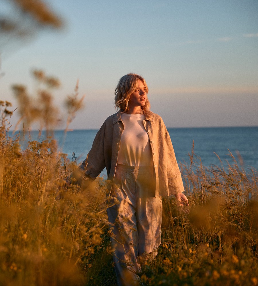 Kvinna går längst med havet i gräset och bär linneplagg