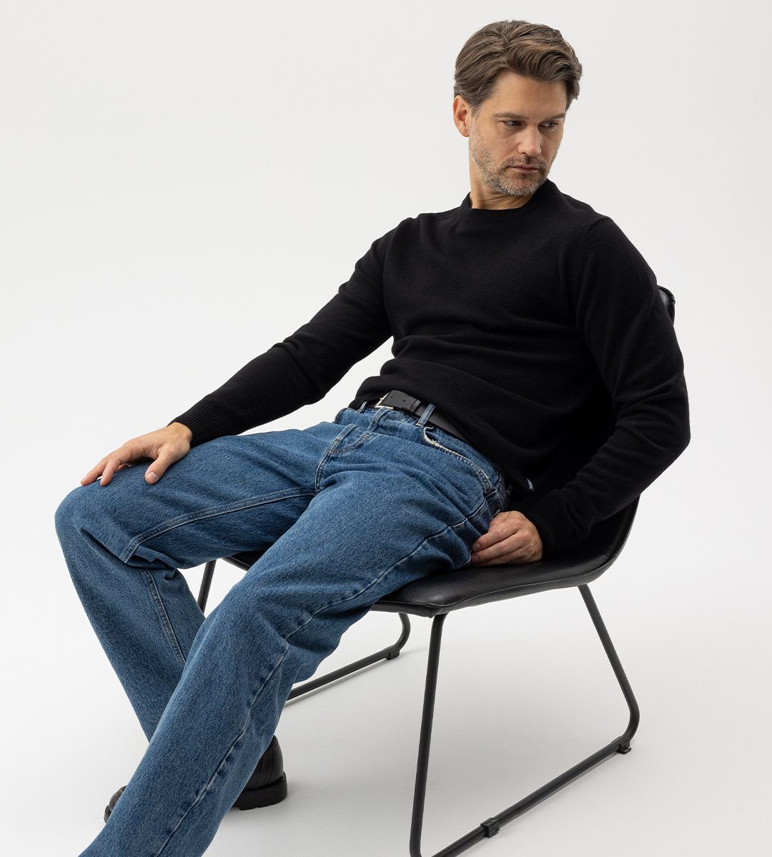 Kille som sitter på stol med jeans och stickad svart tröja