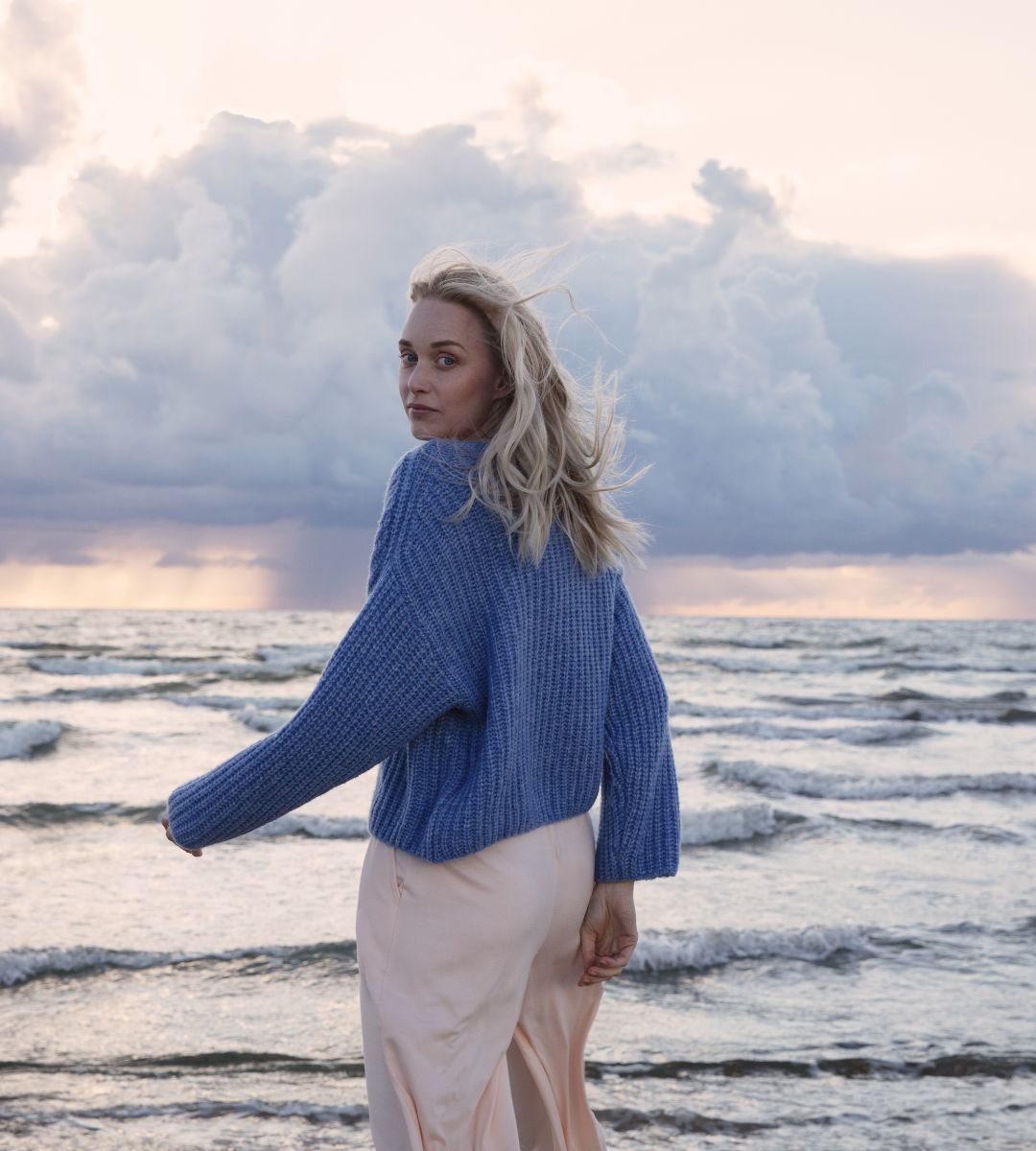 Tjej vid havet som har en blå stickad tröja på sig