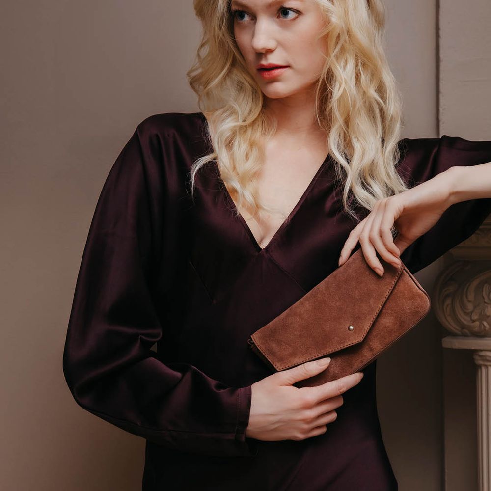 Brun clutchväska mocka skinn som hålls i handen av en person klädd i mörk outfit. House of Nordic