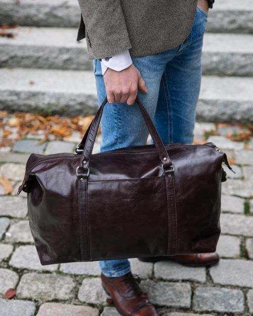 Mann med jeans holder en mørkbrun skinnbag