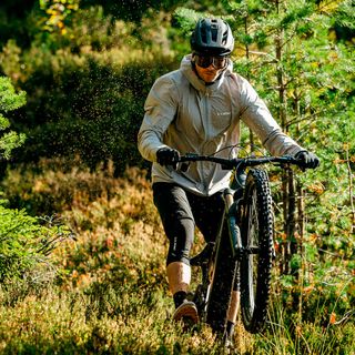 Aurinkolasipäinen mies ajaa Cube-maastopyörällä eturengas ilmassa metsässä.