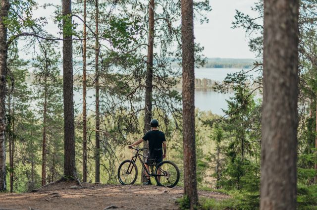 Maastopyöräilijä metsässä katsoo järvelle päin.