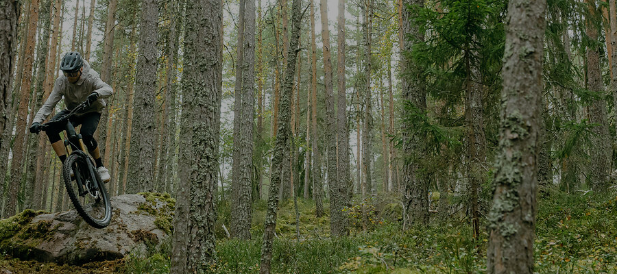 Mies ajaa Cube-maastopyörällä suuren kiven yli tiheässä metsässä. 