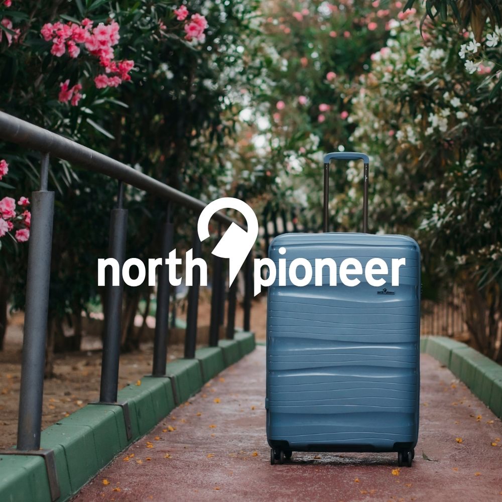 North Pioneer koffert i blått plassert på en sti omgitt av grønt og rosa blomster, med North Pioneer-logoen i hvitt over bildet