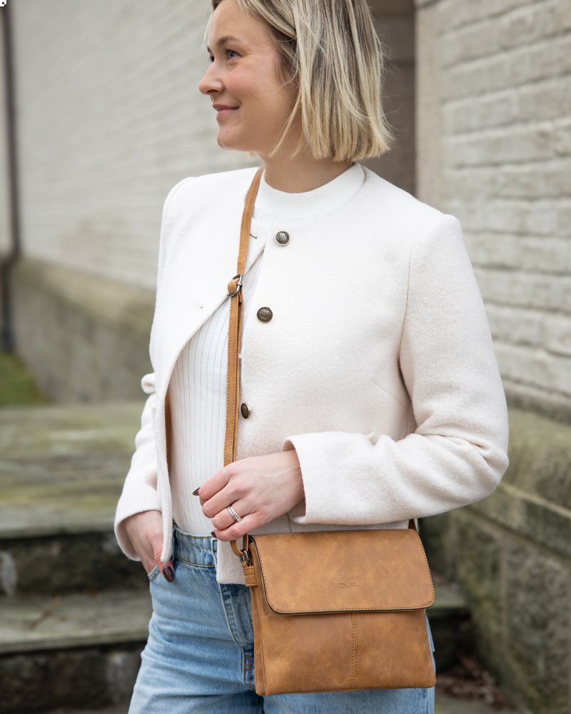 Dame utendørs i lys cardigan og jeans. hun har på en liten crossbody veske i cognac-farge fra Duffy. 