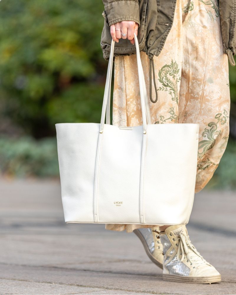 Dame med blomsterkjole som holder en lys toteveske