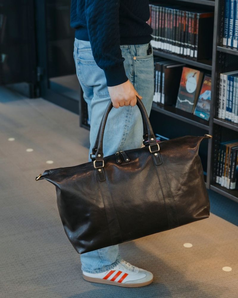 Mann med jeans holder en brun skinnbag inne på et bibliotek
